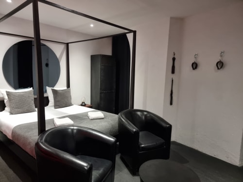 Chambre moderne à Bayeuzen avec lit à baldaquin noir, fauteuils en cuir et décoration minimaliste à Bayeux