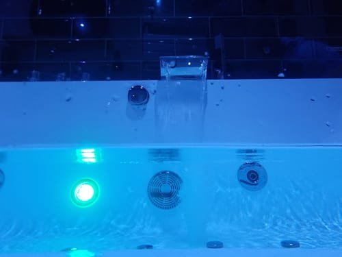 Piscine spa illuminée à Bayeuzen avec éclairages verts scintillants et jets d'eau, présentée dans l'appartement Le Baldaquin