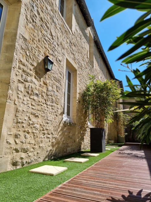 Allée du jardin de la villa en pierre du gîte Bayeuzen avec terrasse en bois, pelouse soignée et plantes tropicales à Bayeux, France
