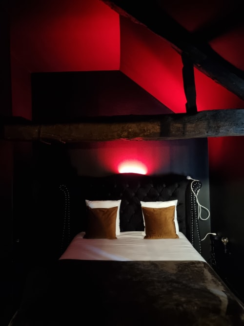 Chambre élégante de la villa Bayeuzen avec éclairage ambiant rouge, literie blanche, oreillers dorés et tête de lit sombre à Bayeux, France
