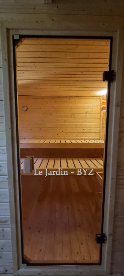 Vue intérieure du sauna en bois de la villa Le Jardin, gîte Bayeuzen à Bayeux, France avec bancs et porte vitrée