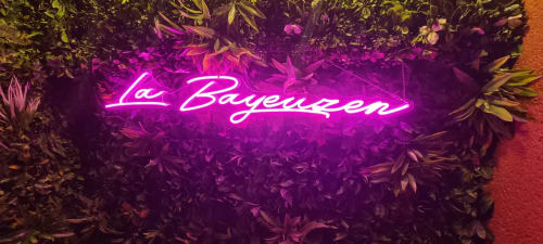 Enseigne néon « la Bayeuzen » aux teintes violettes éclatantes, entourée de végétation tropicale à l'hôtel-boutique Bayeuzen de Bayeux