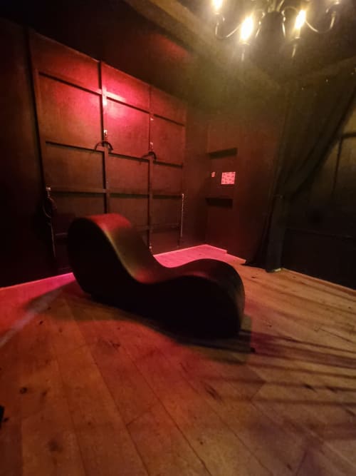 Chaise longue design incurvée dans l'espace spa aux lumières rouges de la villa Bayeuzen à Bayeux, avec sol en bois et accessoires muraux