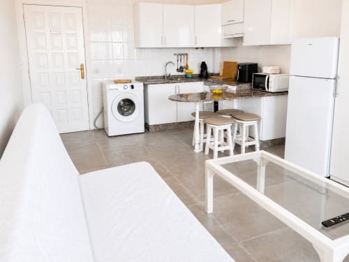 Moderna cocina y comedor del apartamento Restinga Vista Mar en Tenerife con muebles blancos, encimeras de granito y barra