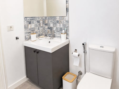 Baño moderno en apartamento de Tenerife con vanidad oscura, lavamanos blanco, inodoro y azulejos decorativos