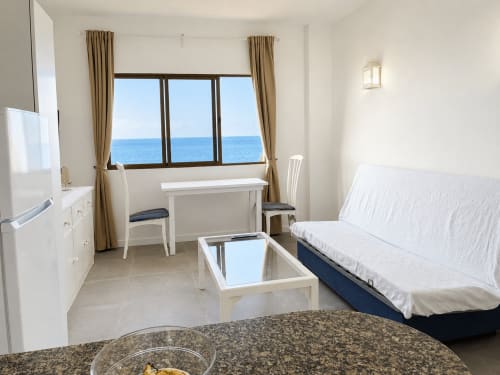 Apartamento luminoso en Tenerife con vistas al mar, mobiliario blanco, cocina americana, sofá cama, escritorio y ventanas con vista al océano