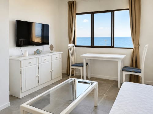 Moderno apartamento luminoso con vistas al mar, muebles blancos, televisión, zona de comedor y océano a través de grandes ventanales en Tenerife
