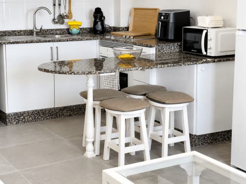 Cocina moderna con encimera de granito, muebles blancos, barra desayunadora y electrodomésticos en apartamento de Tenerife