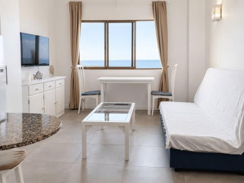 Luminoso apartamento con vistas al mar en Tenerife, salón amueblado, muebles blancos, sofá, zona de comedor y vistas al océano