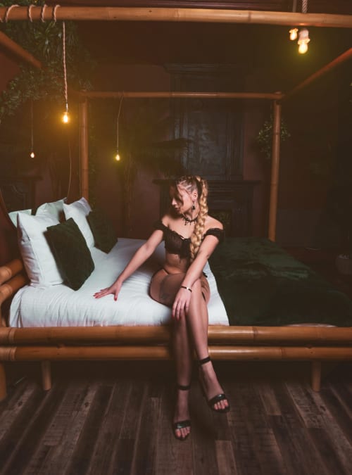 Femme sur lit en bambou à la villa La Tropicale du gîte Bayeuzen à Bayeux, avec luminaires suspendus et décoration vert foncé