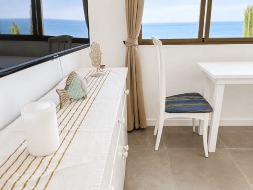 Luminoso apartamento costero con vistas al mar, muebles blancos, alfombra a rayas doradas y océano visible a través de las ventanas