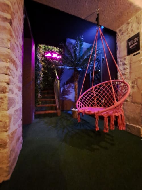 Chaise suspendue rouge sur la terrasse de la villa La Tropicale à Bayeux, illuminée par des néons la nuit