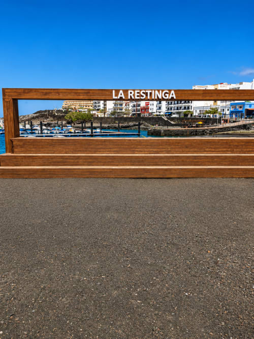 Cartel de La Restinga enmarcando el puerto de Santa Cruz de Tenerife con botes azules y edificios costeros bajo cielo despejado
