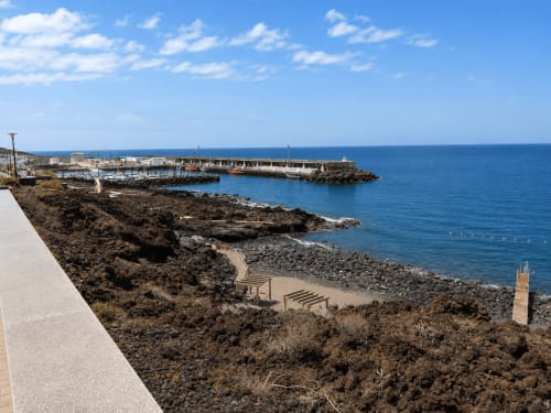 Costa volcánica rocosa con escaleras de acceso a playa y puerto deportivo, vista al mar de Santa Cruz de Tenerife