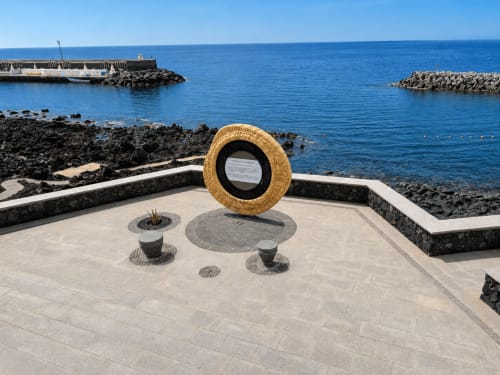 Paseo marítimo con escultura de neumático dorado frente a la costa rocosa y puerto de Santa Cruz de Tenerife