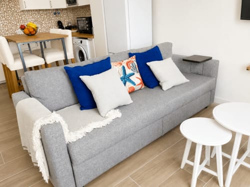 Moderno salón con sofá gris, cojines decorativos y mesitas blancas en apartamento de Tenerife con vistas al mar
