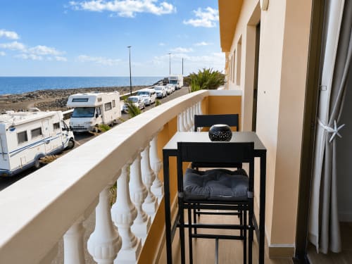 Balcón con silla negra frente al mar y autocaravanas estacionadas en Tenerife, apartamento con vistas al océano
