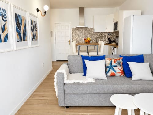 Moderno salón en Tenerife con sofá gris, detalles azules, cocina y vistas al mar