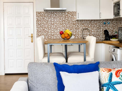 Moderna cocina de apartamento en Tenerife con azulejos geométricos, mesa de comedor, sillas blancas y sala de estar colorida