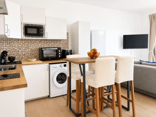 Cocina-comedor moderno en apartamento de Tenerife con encimera de madera, lavadora, microondas, mesa de comedor y sillas