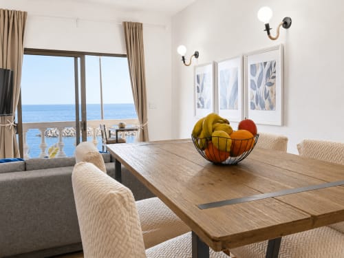 Luminoso comedor de apartamento frente al mar en Tenerife con mesa de madera, vistas al océano y mobiliario moderno