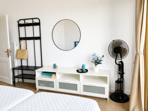 Dormitorio moderno con armario blanco, espejo redondo, perchero negro y ventilador en Santa Cruz de Tenerife