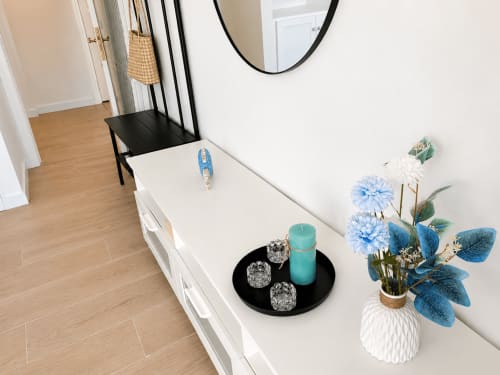 Recibidor moderno con consola blanca, silla negra, flores decorativas azules y piso de madera en Santa Cruz