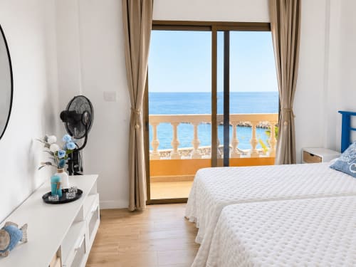 Luminoso dormitorio de apartamento frente al mar en Tenerife con balcón vista al océano, cama blanca, suelos de madera y terraza