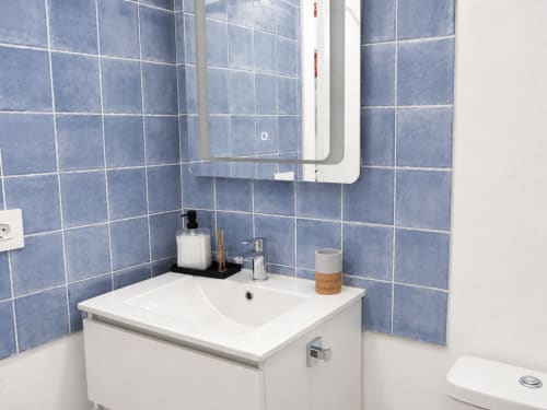 Lavabo moderno con vanidad blanca, paredes azulejos azules y espejo en apartamento de Tenerife