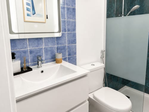 Baño moderno en apartamento de Tenerife con azulejos azules, lavabo blanco, inodoro y ducha de cristal