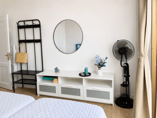 Moderno dormitorio de apartamento en Santa Cruz de Tenerife con muebles blancos, estantería negra, espejo redondo y ventilador