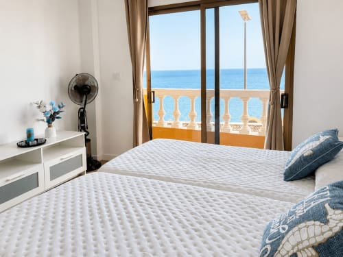 Luminoso dormitorio frente al mar en Tenerife con camas gemelas, vistas al océano a través de puertas acristaladas y balcón con vista al mar
