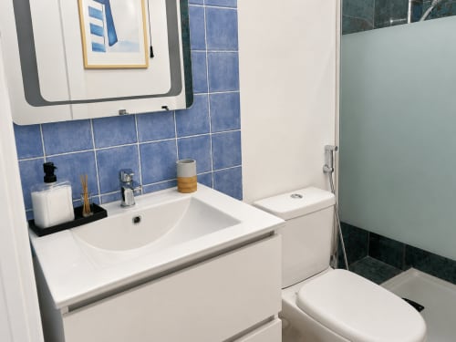 Baño moderno en apartamento de Tenerife con lavabo blanco, inodoro, revestimiento azul y botiquín espejo