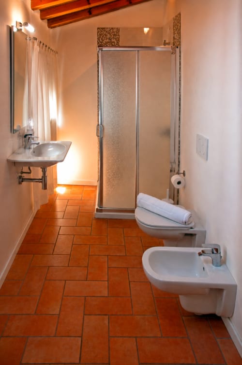 Bagno moderno a Corte delle Giuggiole B&B con pavimento in cotto, box doccia in vetro, sanitari bianchi