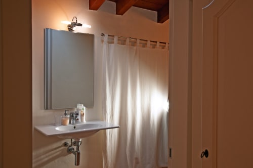 Bagno moderno nella camera del B&B Corte delle Giuggiole con lavabo a parete, specchio, illuminazione del mobile e tenda doccia bianca