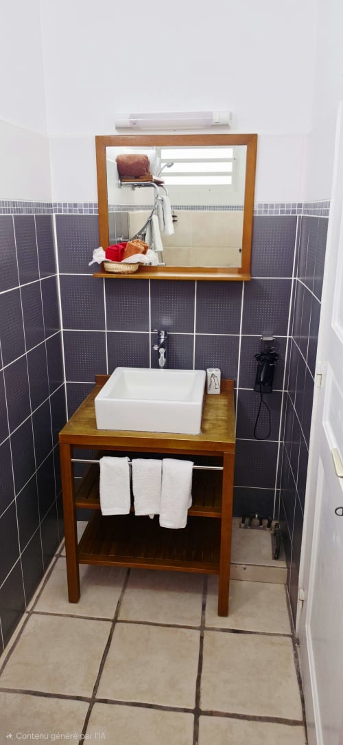 Salle de bain moderne avec lavabo blanc, miroir en bois et murs en carrelage foncé au gîte Le Nid De Bellemont à Trois-Rivières