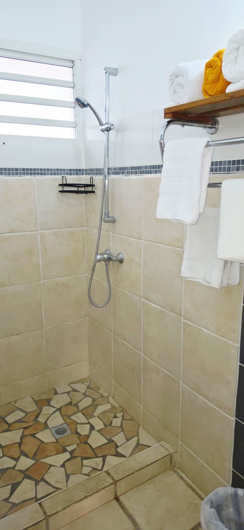 Salle de bain moderne avec carrelage beige, pomme de douche pluie et serviettes blanches du gîte bord de mer Le Nid De Bellemont