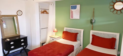 Chambre vert vif au Le Nid De Bellemont avec lits jumeaux, oreillers rouges, commode noire et miroir à Trois-Rivières