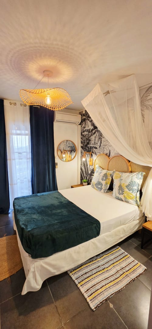 Chambre élégante au Nid De Bellemont avec lit à baldaquin, lampe suspendue tissée, papier peint tropical et vue sur mer