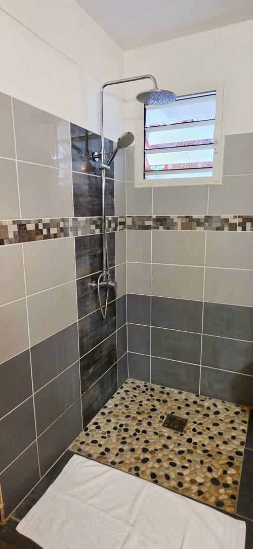 Salle de bains moderne au gîte Le Nid De Bellemont avec douche à effet pluie, carrelage mosaïque et fenêtre