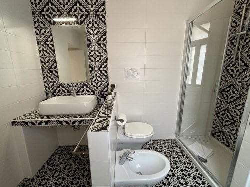 Bagno moderno a Domus Caecilia Roma con piastrelle geometriche bianche e nere, lavabo, wc, bidet e doccia