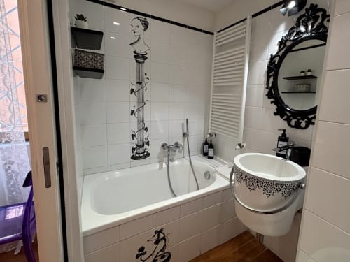 Bagno elegante presso Domus Caecilia Roma con piastrelle bianche, opere d'arte decorativa nera, specchio rotondo, lavabo su colonna e vasca