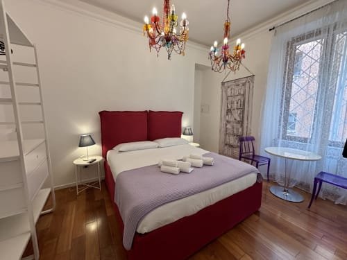 Camera elegante a Domus Caecilia Roma con letto bordeaux, lampadari in cristallo, pavimenti in legno e comfort moderni.