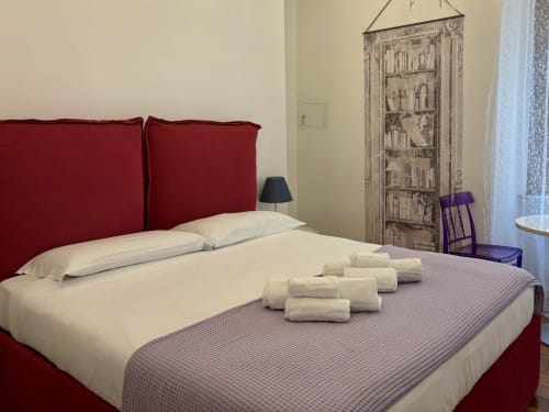 Camera luminosa della Domus Caecilia Roma con testata rossa, biancheria bianca e asciugamani arrotolati su plaid texturizzato
