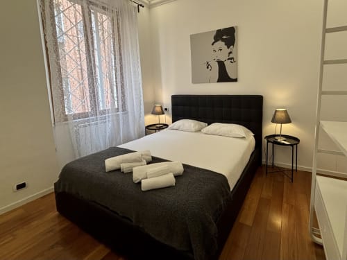 Camera moderna a Domus Caecilia Roma con letto nero, biancheria bianca, lampade comodino, pavimenti in legno e opere d'arte.
