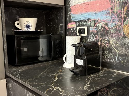 Angolo cucina a Domus Caecilia Roma con bancone in marmo nero, microonde Sharp, macchina caffè e bollitore.