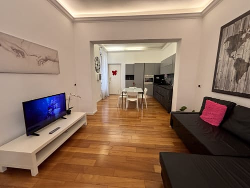 Elegante zona living con divano nero, TV, pavimenti in legno e cucina a vista presso l'hotel Domus Caecilia a Roma