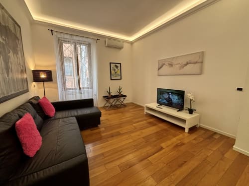Soggiorno moderno dell'appartamento Domus Caecilia a Roma con divano nero, pavimenti in legno, TV e arredamento contemporaneo
