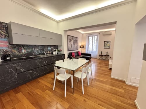 Moderno appartamento open-plan a Roma con cucina in marmo nero, tavolo da pranzo bianco e soggiorno con divano nero