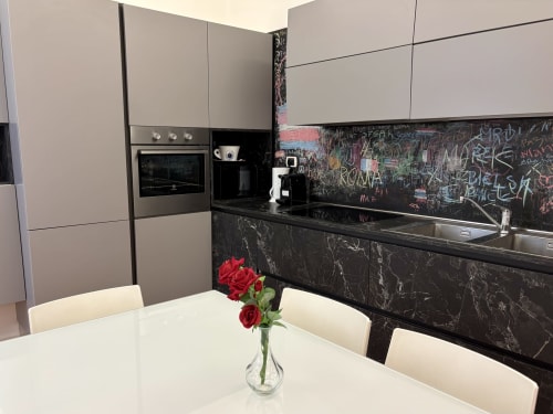 Cucina moderna dell'appartamento Domus Caecilia a Roma con tavolo da pranzo bianco, rose rosse e schienale in lavagna